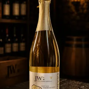 Sektflasche Jungwinzersekt 2022 auf einer edlen schwarzen Schieferplatte in einem Weinkeller.